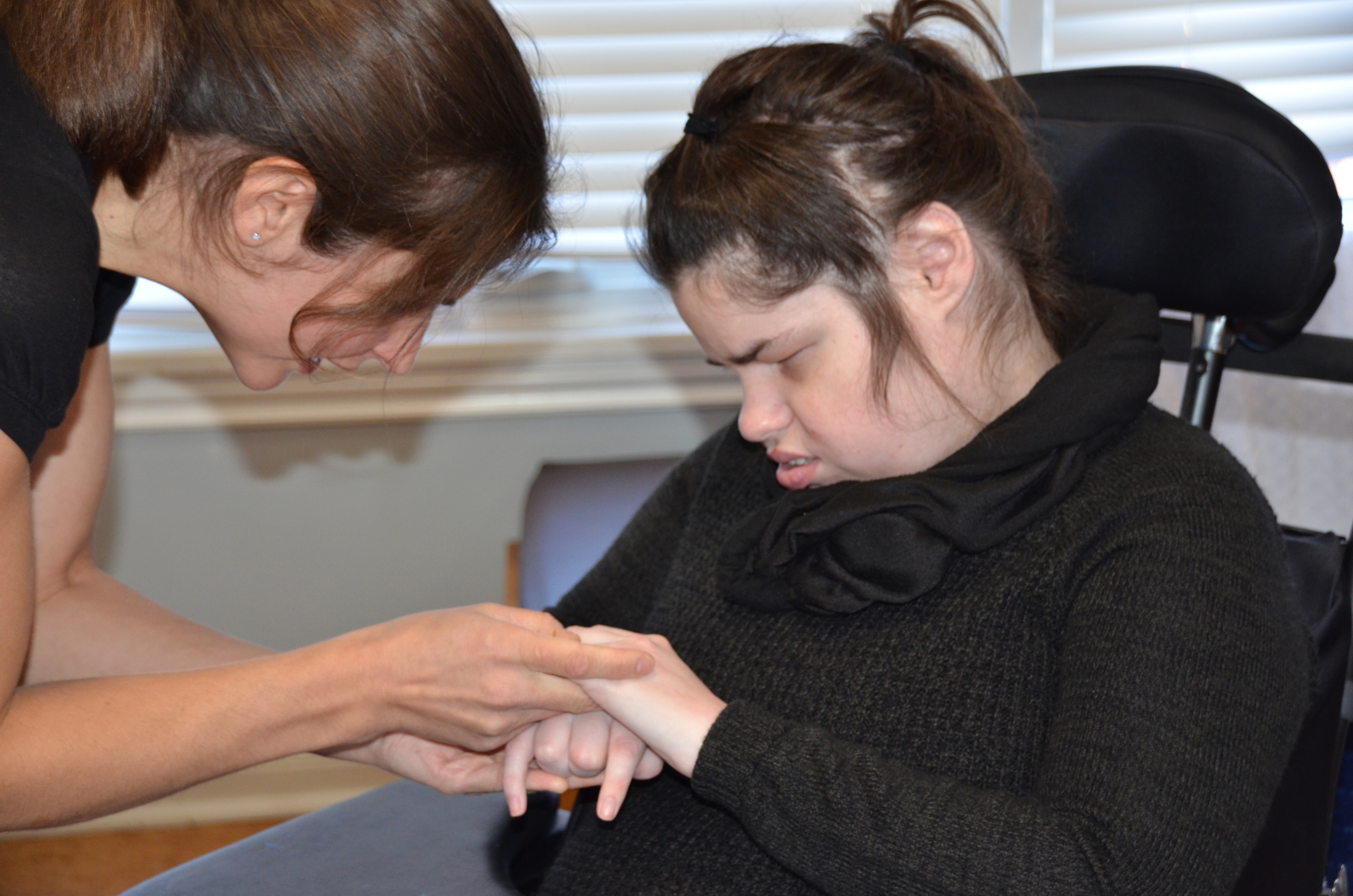 A woman with deafblindness in a wheelchair communicates with her intervenor using AITSL, a hand-over-hand sign language.