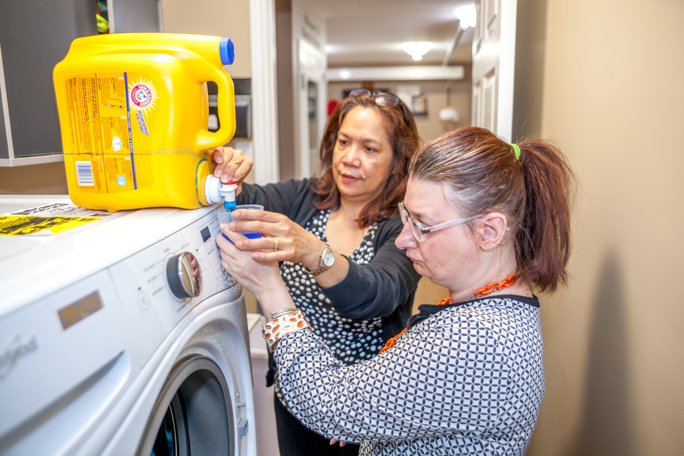 Intervenor assists woman with pouring laundry detergent, supporting her in doing laundry more independently.
