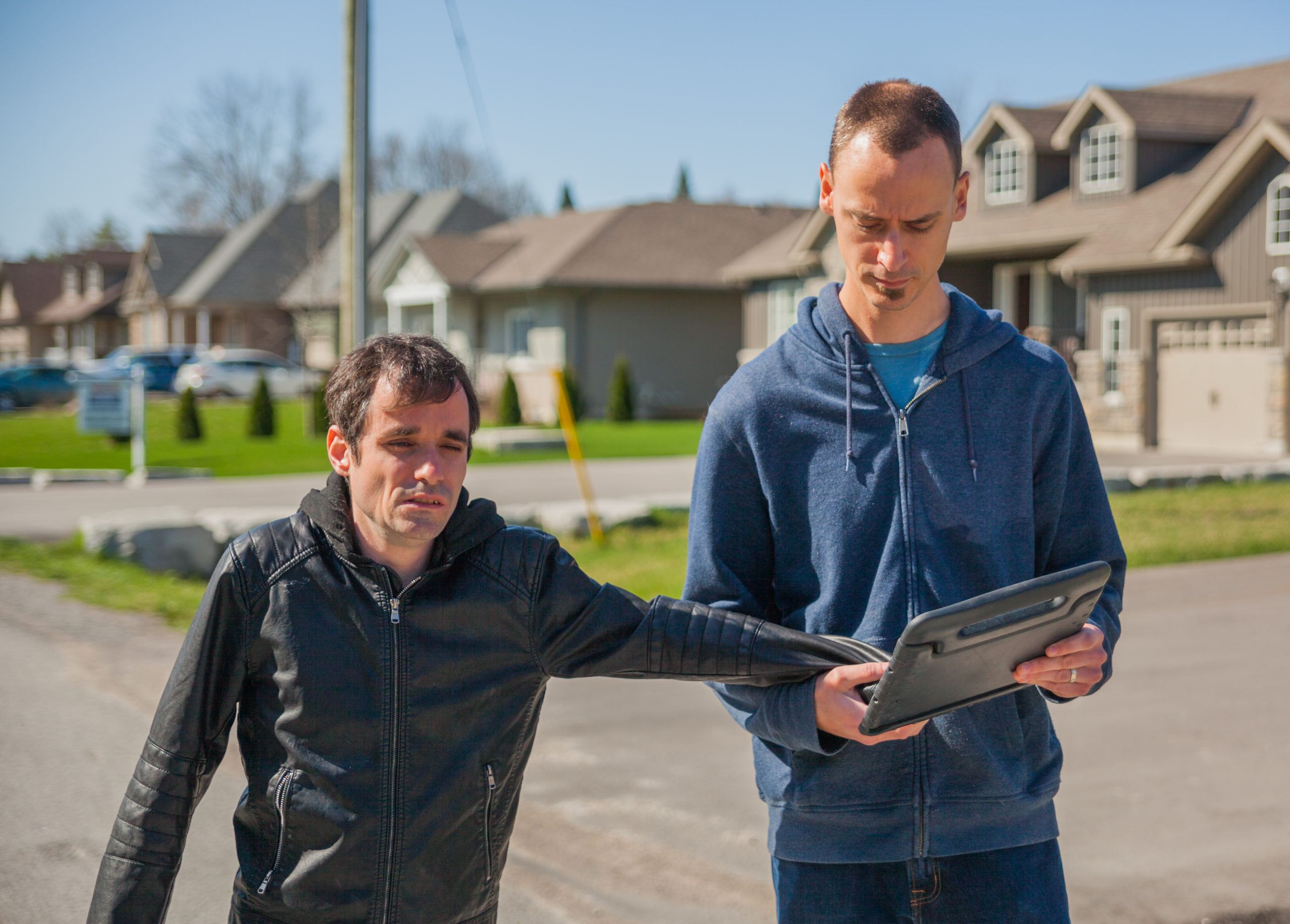 L’interprète tactile communique avec un homme à l’aide d’un iPad. Ils se promènent dehors dans un quartier résidentiel.