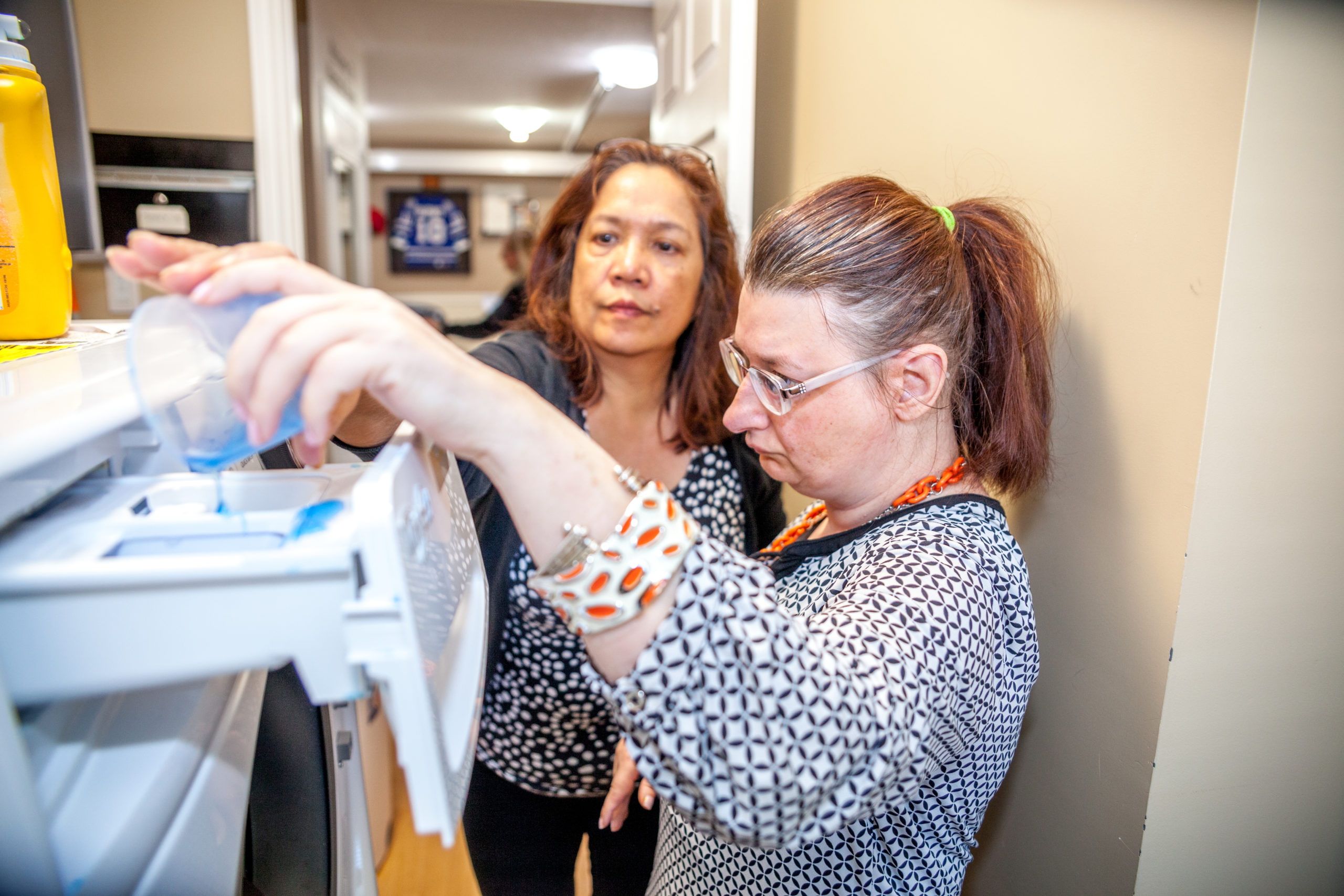 Intervenor assists woman with pouring laundry detergent.