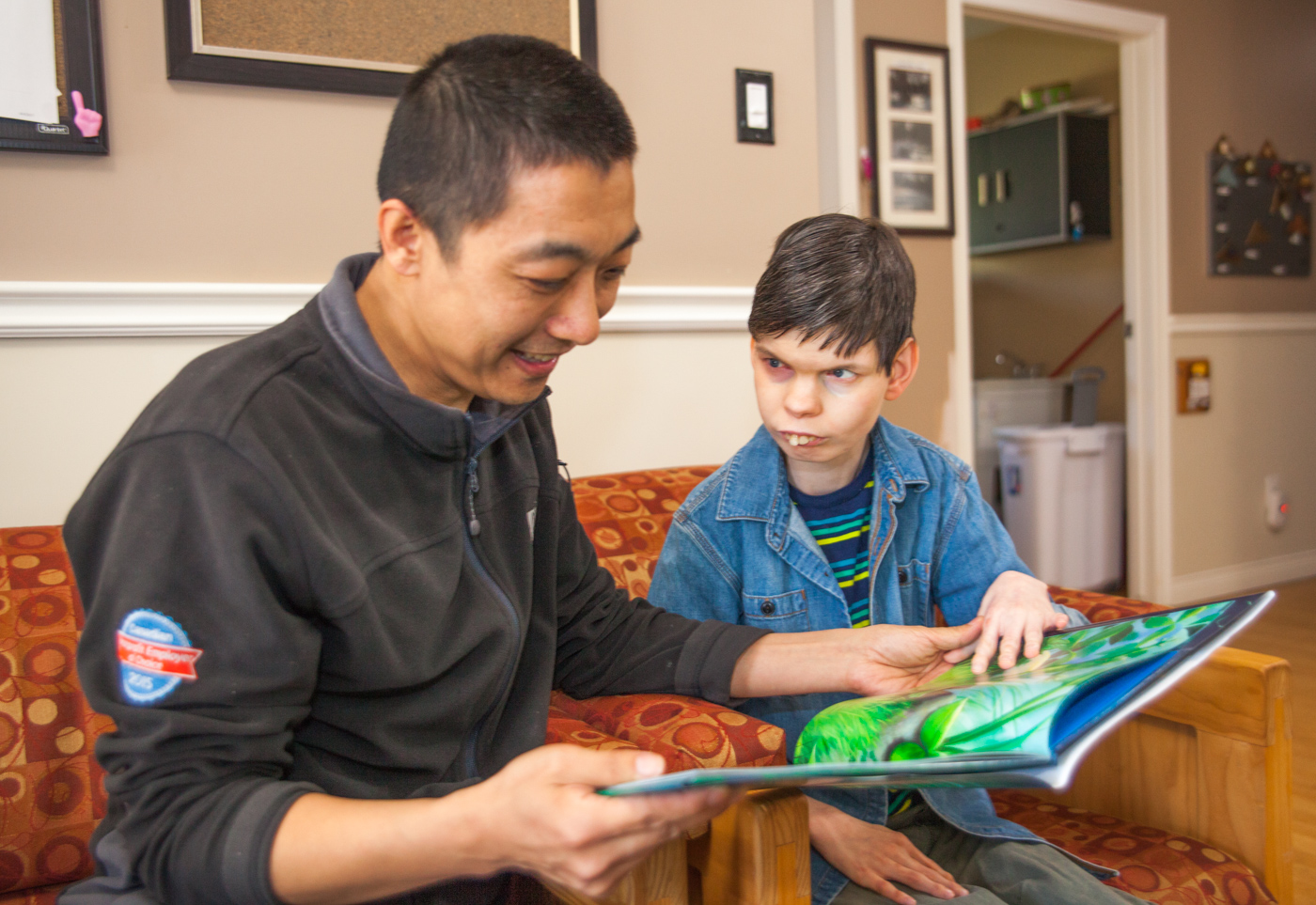 Intervenor and young man supported sit on a couch, reading a large book with pictures.