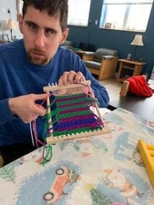Man wearing blue shirt holding a loom of yarn