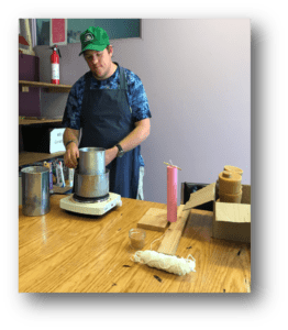 Man wearing a green hat and navy apron making beeswax candles