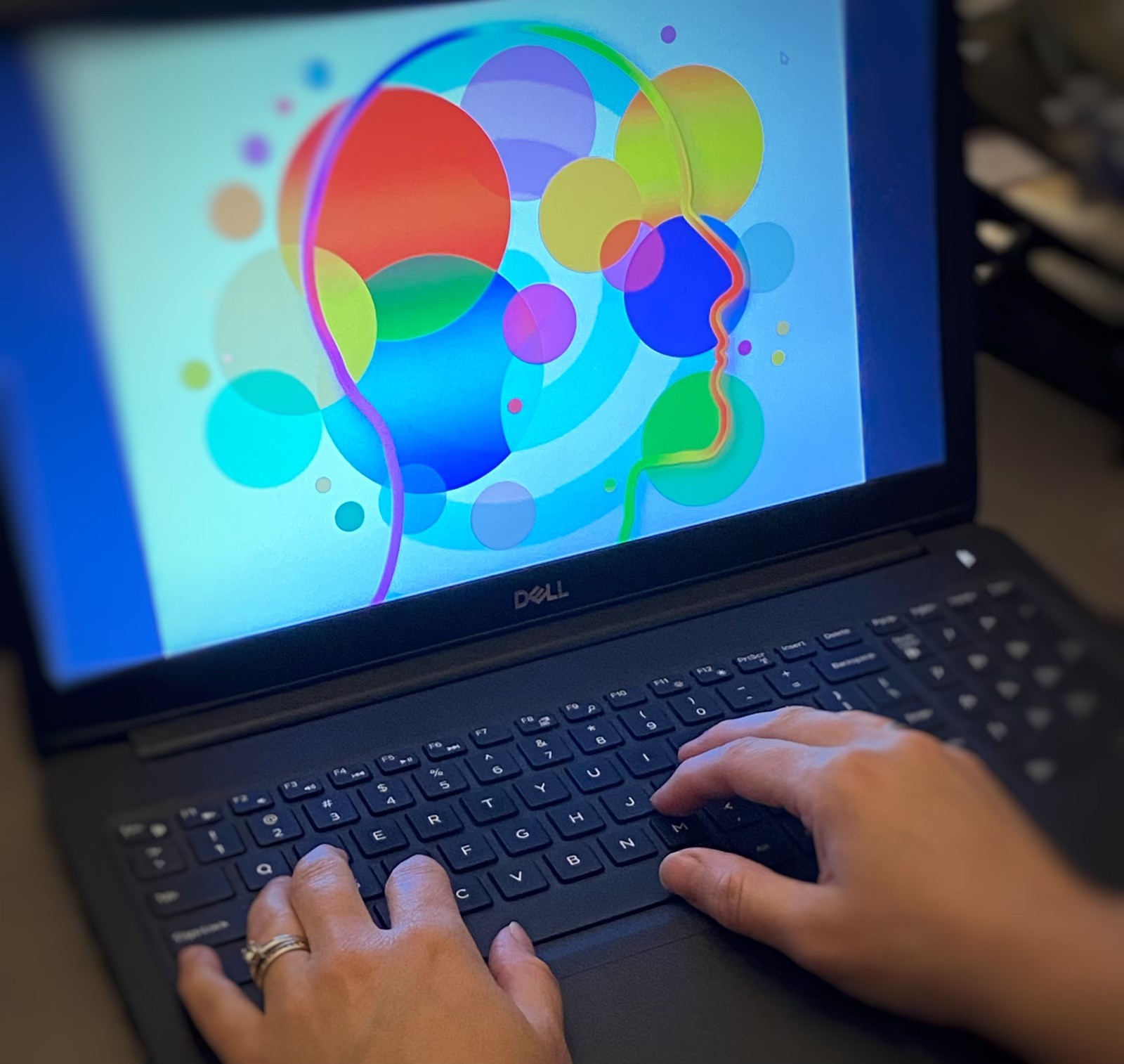 Laptop computer with colourful balls on screen and two hands resting on the keyboard