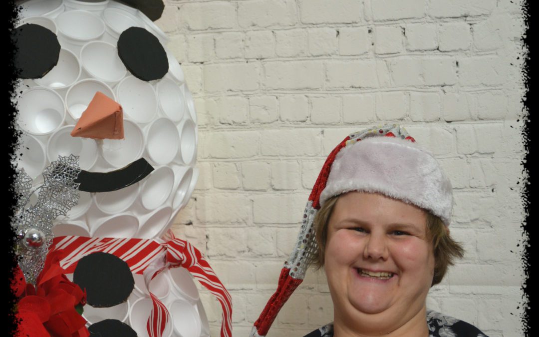 image of woman smiling, wearing a Santa hat, next to a snowman