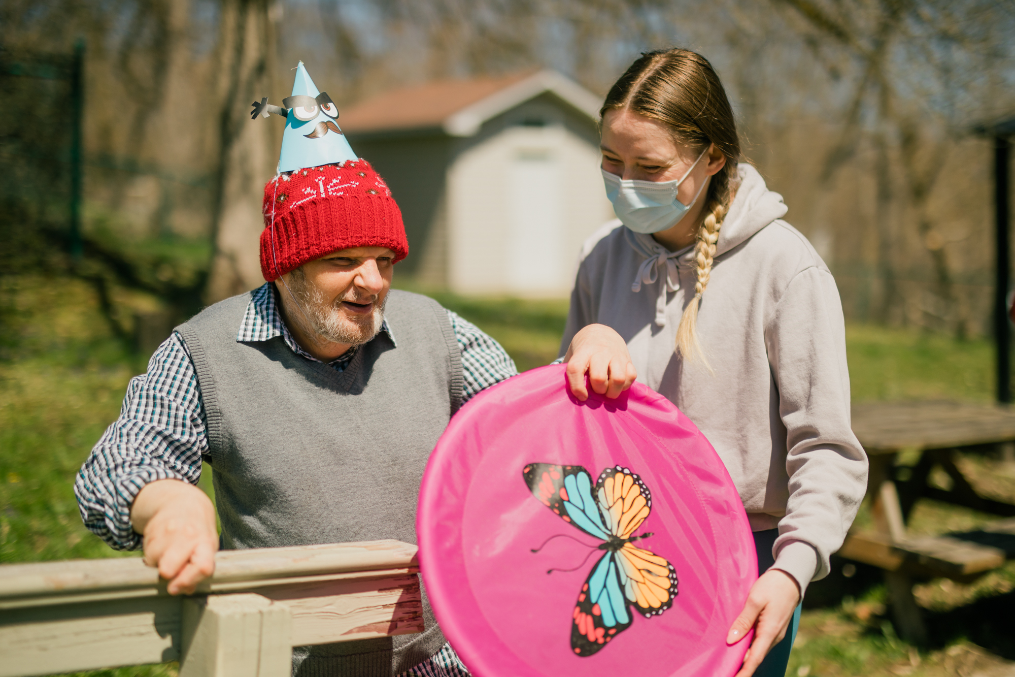 Image of woman wearing a surgical mask holding a pink frisbee next to a man in a party hat